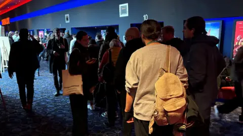 A photo showing people queuing in a low-lit cinema foyer