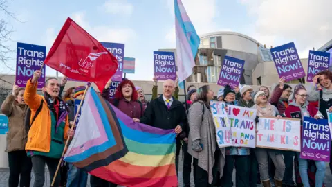 Getty Images Trans rights campaigners outside the Scottish Parliament, holding up a flag in their colours, and placards reading 