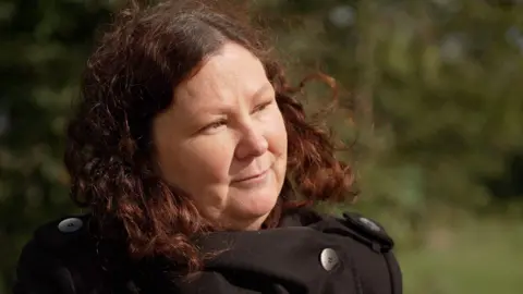 BBC  Cassandra Wardle looks off frame with a black coat in a countryside background