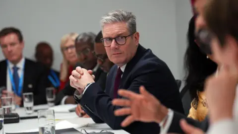 Getty Images UK Prime Minister Keir Starmer attends a financial meeting with international colleagues as part of the COP29 climate conference meeting on 12 November, 2024 in Baku, Azerbaijan. He is in the centre of the image, wearing a dark suit and has his hands clasped together