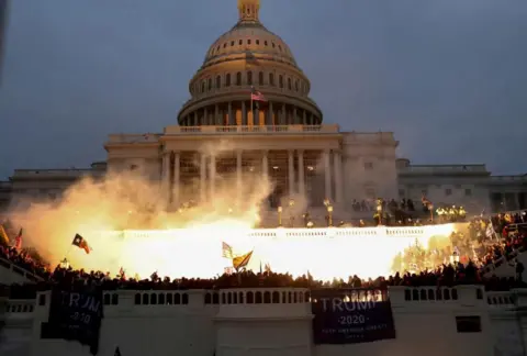 Reuters An explosion caused by a police munition lights up the front of the US Capitol building in Washington on 6 January 2021. Trump supporters are gathered there.