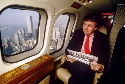 Getty Images Donald Trump reads the newspaper in his helicopter while flying over the Twin Towers in New York .