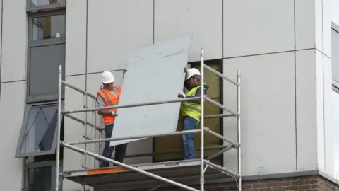 Getty Images Image showing two workmen in white hardhats and hi-vis vests removing external cladding from Burnham Tower on the Chalcots Estate in Camden in 2017