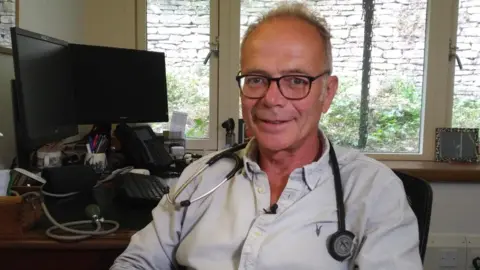 Dr Simon Opher in his GP surgery with a stethoscope round his neck