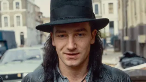 Getty Images A head and shoulders archive shot from 1984 of Bono in a big black-rimmed hat arriving at the recording studio.