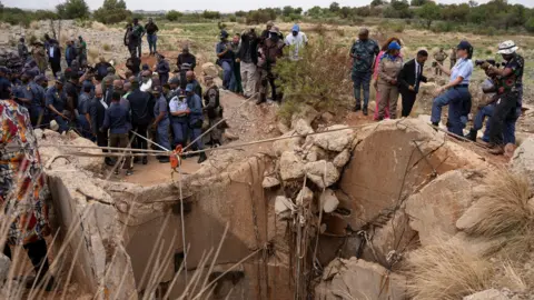 Reuters Community members watch as Senzo Mchunu, South Africa's police minister, inspects outside the mineshaft where it is estimated that hundreds of illegal miners are believed to be hiding underground.