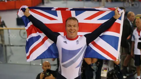 Getty Images Chris Hoy in his cycling outfit holds behind him the Union flag following a win at the London 2012 Olympics