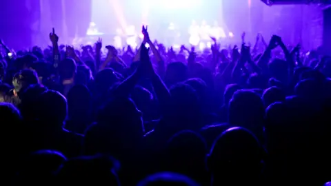 Getty Images A picture taken behind the crowd at Warehouse project in Manchester with their hands in the air looking towards the stage.