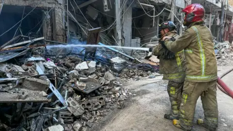 AFP via Getty Images Emergency workers putting out a fire with a hose following an Israeli strike in southern Beirut