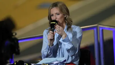 Getty Images Gabby Logan presenting while holding a microphone. She has blonde long hair and is wearing a light blue shirt.