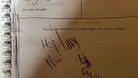 Family handout A page of a lined notebook. At the top it says 'Journal prompt: What specific situations or thoughts trigger your anxiety, and why?'. Underneath are scrawled the words 'Help Me' and 'Lucy' in black biro