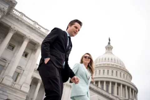 Getty Images Matt Gaetz and his wife Ginger Gaetz walk down the steps of the House of Representatives in Washington DC. The two are holding hands, with Matt Gaetz in a dark suit and Ginger Gaetz in a mint suit.