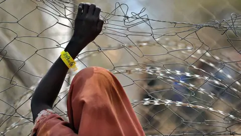 AFP A newly registered Somali refugee supports herself on a chain-link perimeter fence outside a registration and medical aid facility at the Dadaab Internally Displaced People (IDP) camp in eastern Kenya on July 23, 2011