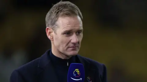 Getty Images Dan Walker wearing a navy jacket and black zipped up top, holding a Premier League navy microphone