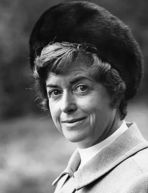 June Spencer in a dark fur hat and plain, lighter coat, in a black and white image