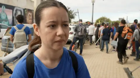 Amparo Esteve in a blue tshirt and with a rucksack speaks to the camera