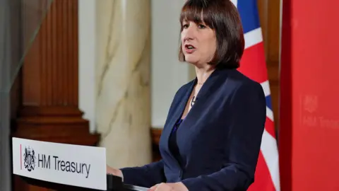 Reuters Rachel Reeves stands at a lectern at the Treasury with a union flag behind her.