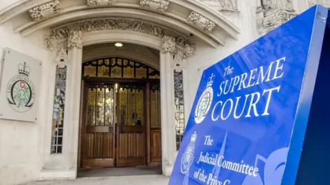 Getty Images Entrance to the Supreme Court in London, a white brick building covered in ornate carvings, including a big blue sign reading 