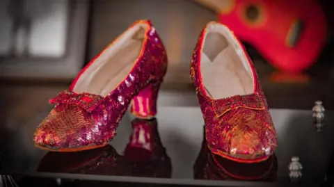 Heritage Auctions A close-up of the ruby red sequin shoes worn by Judy Garland. They feature dark red sequins sewn in chevron strips across the front of the shoes, with red bows sewn on and thick block heels at the back, with a light coloured insole