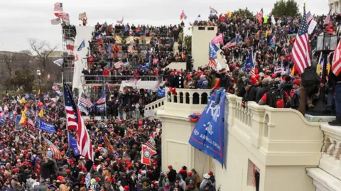 Reuters Seen at a distance and from the side, supporters of then-US President Donald Trump gather are seen covering the front steps of the Capitol building on 6 January. They are holding American and Trump flags