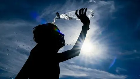 EPA Boy pours water over himself during a heatwave, with the sun in the background.