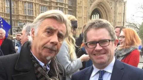 Kevin Brennan Sex Pistol Glen Matlock and former Cardiff West MP Kevin Brennan at a demonstration surrounded by other people outside the Houses of Parliament. Both are dressed smartly and looking at the camera