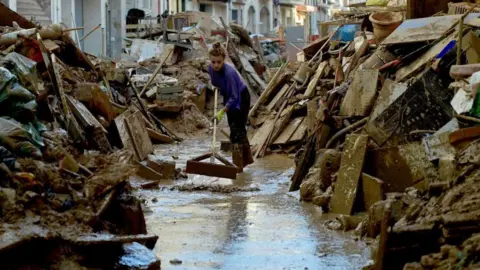 Getty Images A woman trying to clear muddy water from a street in the town of Paiporta, south of the city of Valencia