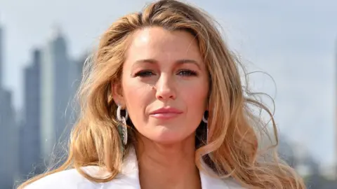 Getty Images Blake Lively in a white suit and earrings posing in front of the London  skyline on 8 August