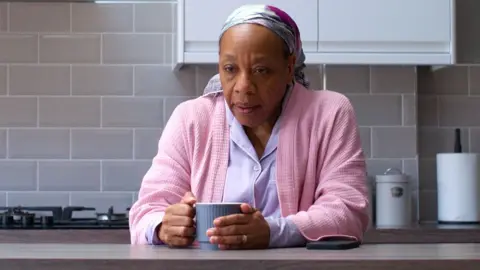 Studio Canal Marianne Jean-Baptiste as Pansy in Hard Truths, sitting at her kitchen counter with a cup of tea, looking exhausted