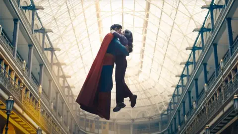 DC Studios/WB Superman and Lois Lane kissing while in mid-air in the middle of an ornate old building in a still from the trailer