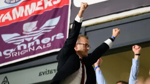 Getty Images Daniel Křetínský pictured holding his arms in the air in celebration while watching West Ham at a football game