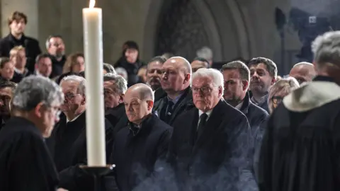 Getty Images Clergymen pass by German Chancellor Olaf Scholz (SPD) (C-L) and German President, Frank-Walter Steinmeier (C-R) during a prayer ceremony at the Magdeburg Dom church