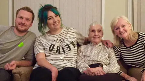 Anne Puckridge Anne with her grandchildren Andrew and Kirsty and daughter Gillian. They are sitting on a sofa and smiling.