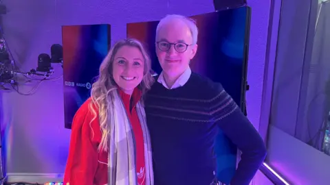 Laura Kenny is dressed in a red coat and scarf next to James Gallagher, who is wearing a blue shirt and jumper. They are standing by the Today programme radio studio. 