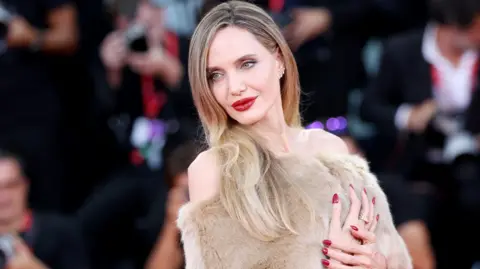 Getty Images Angelina Jolie in a faux fur dress against a backdrop of photographers