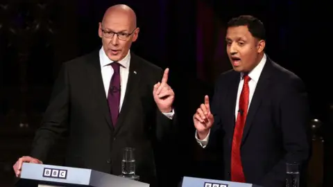 Getty Images John Swinney and Anas Sarwar at a BBC election debate, both with mouths open in mid sentence and their fingers held aloft