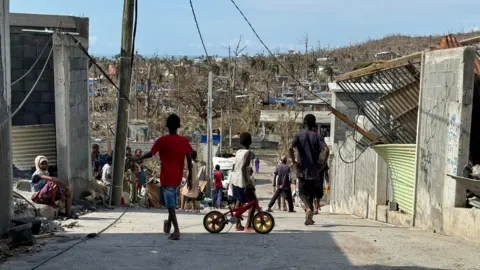 BBC/Ed Habershon Children in the foreground on a road with damaged buildings behind