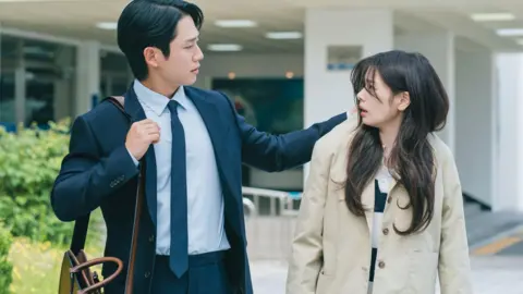 Netflix A scene from the K-drama, Love Next Door, where the male lead grabs the coat of the female lead, while they both are walking down a street 