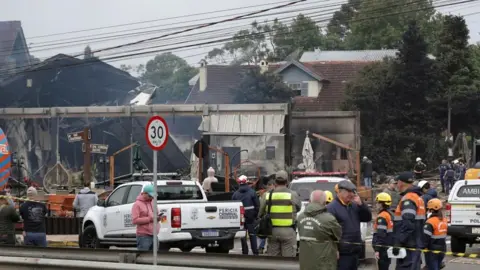 Reuters Emergency workers attend burned out buildings behind police tape at the scene of the crash.