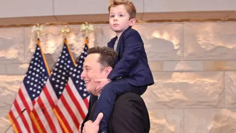 Getty Images Tesla CEO Elon Musk, co-chair of the newly created Department of Government Efficiency (DOGE), carries his son 