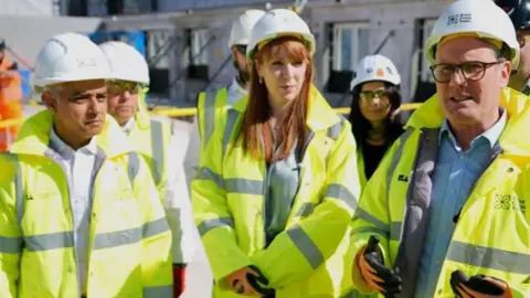 PA Media Sadiq Khan, Angela Rayner and Sir Keir Starmer wearing hi-vis jackets and white hard hats on a building site