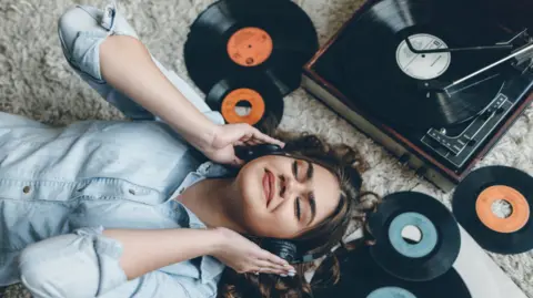 Getty Images Woman lying on the floor, smiling as she listens to records.