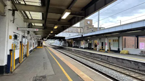 Ben Schofield/BBC A look along a near-deserted platform at Luton station, with tracks sweeping away into the distance, from bottom right into the middle-left of the image. The station's 1930s clock tower is just visible in the background, as is a footbridge over the tracks.