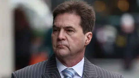 Getty Images Craig Wright, a white man in his fifties with short brown hair. He is wearing a sharp pinstripe suit with a striped tie and white shirt.