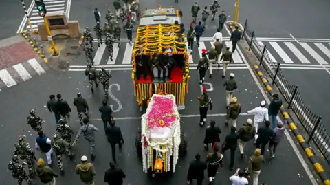 AFP via Getty Images Funeral procession shows several people walking behind a coffin covered in colourful flowers on a street in New Delhi