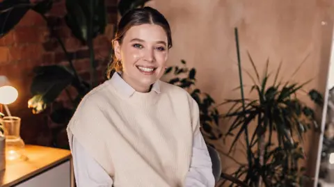 Isobel Perl Isobel wearing a white shirt and cream jumper smiles directly at the camera