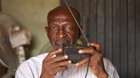 Ifiokabasi Ettang / BBC Bala Muhammad holding a radio in his shop