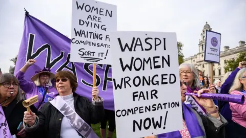 Getty Images Protesters from the Women Against State Pension Inequality (Waspi) group demonstrate outside Parliament in London. They are wearing purple sashes and holding signs reading: 