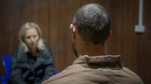 BBC/Matthew Goddard Al Sina IS inmate sits with his back to the camera, facing reporter Orla Guerin who is out of focus