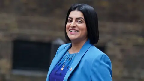 PA Media Shabana Mahmood wearing a bright blue jacket and dress smiles at the camera as she walks into Downing Street.